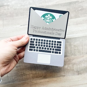 May include: A gray laptop-shaped gift card holder with a black keyboard design and the text "Happy Administrative Professional's Day." The holder contains a Starbucks gift card with the company's logo.