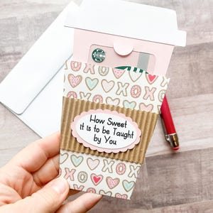 May include: A brown paper cup gift card holder with a pink lid and a white envelope. The cup has a pattern of pink and blue hearts and the text "How Sweet it is to be Taught by You".