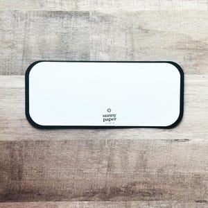 Peut inclure: Une carte rectangulaire blanche aux coins arrondis et bord&eacute;e de noir. La carte porte le texte "sunny paper studio" et un petit logo en forme d'&eacute;clat de soleil dans le coin inf&eacute;rieur droit. La carte est sur une surface en bois.