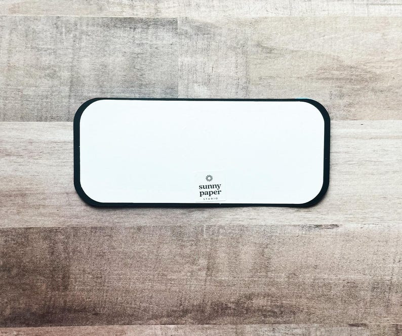 Peut inclure: Une carte rectangulaire blanche aux coins arrondis et bord&eacute;e de noir. La carte porte le texte "sunny paper studio" et un petit logo en forme d'&eacute;clat de soleil dans le coin inf&eacute;rieur droit. La carte est sur une surface en bois.