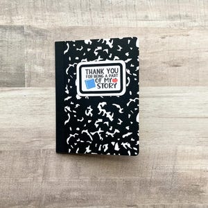 May include: A black composition notebook with a white and black abstract pattern. A white rectangle with the text "THANK YOU FOR BEING A PART OF MY STORY" is on the front, with a book and apple graphic.