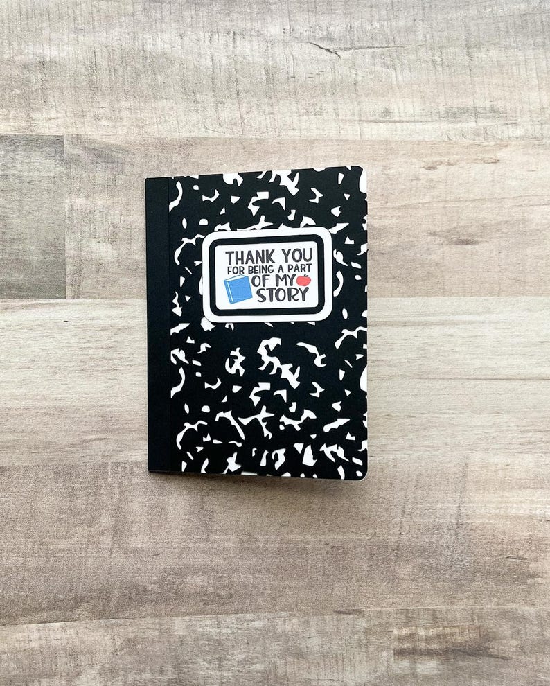 May include: A black composition notebook with a white and black abstract pattern. A white rectangle with the text "THANK YOU FOR BEING A PART OF MY STORY" is on the front, with a book and apple graphic.