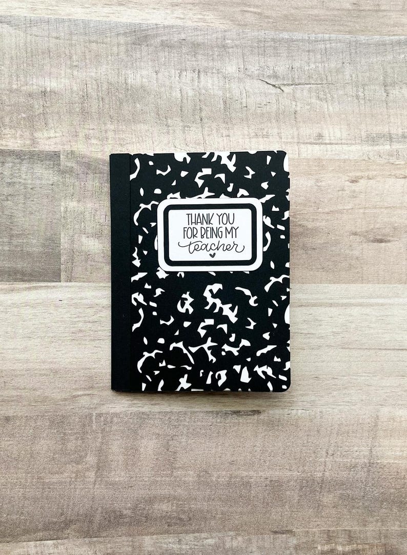 May include: A small, black and white composition notebook with a unique pattern. The notebook features a white rectangular label with the text "THANK YOU FOR BEING MY TEACHER" in black script. A heart is below the text.