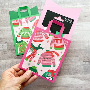 May include: Gift card holders in green and pink, shaped like shopping bags. The bags feature a pattern of holiday sweaters in red, green, and pink. One bag is open, revealing a gift card. The text on the gift card reads "$15-$500".