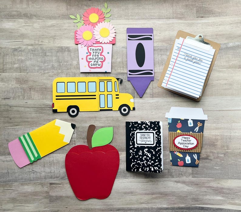 May include: A collection of colorful, die-cut paper crafts with a school theme. Includes a yellow school bus, a red apple, a pencil, a crayon, a notepad, a coffee cup, a notebook, and a flower pot with the text "Thank you for helping me grow."