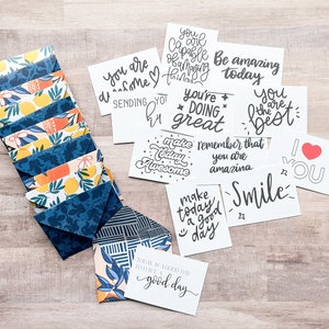May include: A stack of colorful cards with positive messages, such as "You are amazing today" and "Make today awesome". The cards are on a wooden surface.