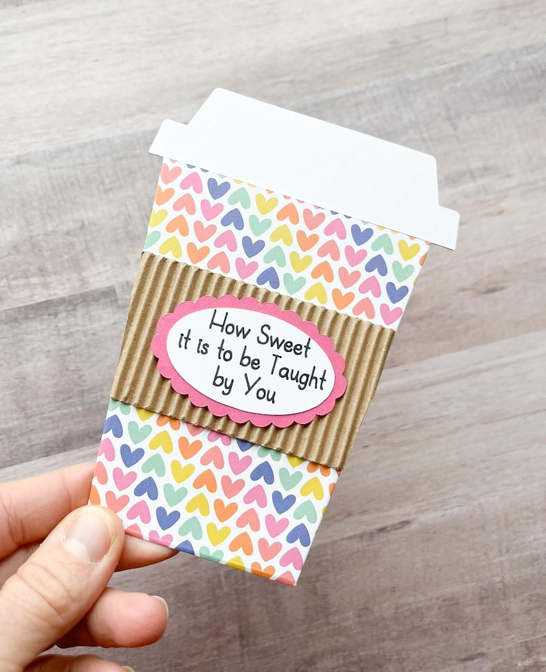 May include: A colorful coffee cup card with a pink oval label that reads "How Sweet it is to be Taught by You". The card is decorated with a pattern of small hearts in various colors.