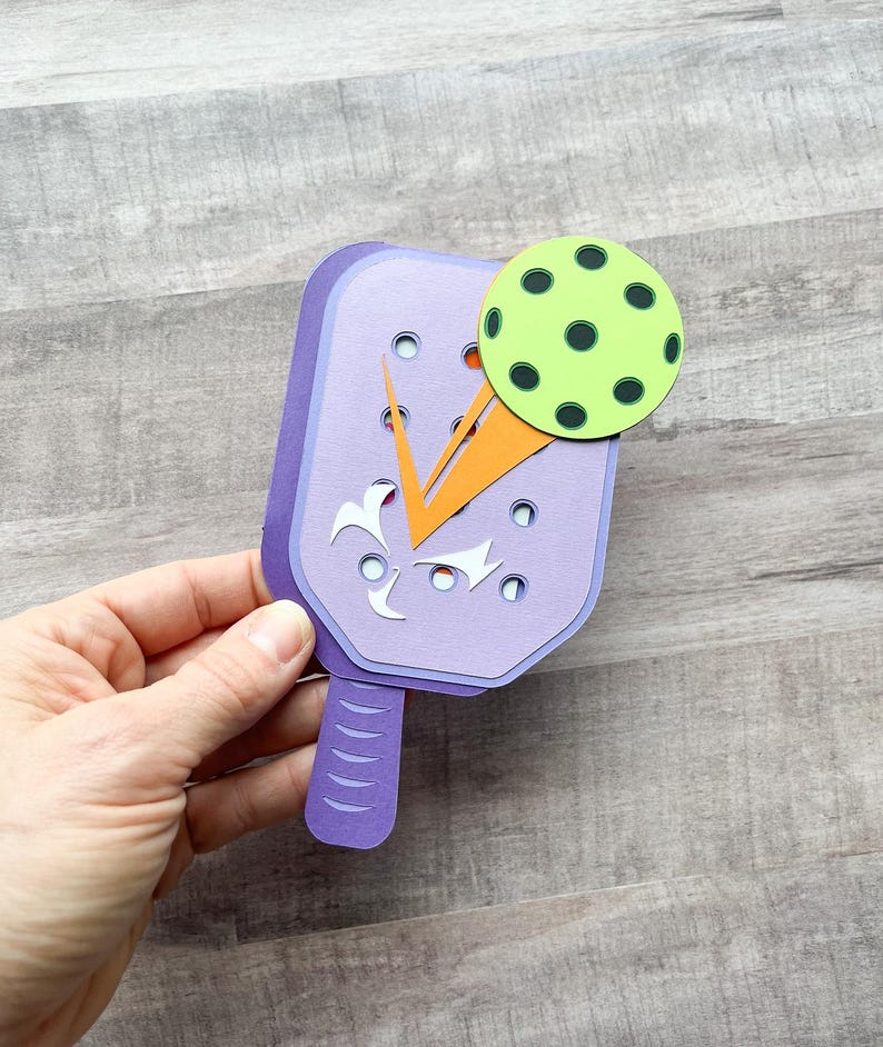 May include: Purple paper craft paddle with an orange and white design and a green and black paper ball.