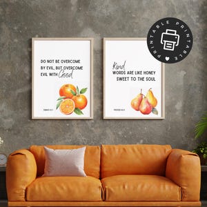 May include: Two rectangular wall art prints in light wood frames. The left print features oranges and the text DO NOT BE OVERCOME BY EVIL, BUT OVERCOME EVIL WITH GOOD ROMANS 12:21. The right print features pears and the text KIND WORDS ARE LIKE HONEY SWEET TO THE SOUL PROVERBS 16:24.