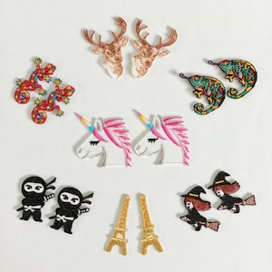 May include: A collection of embroidered patches featuring various designs. Included are two deer heads, two colorful geckos, two unicorns with pink manes, two ninjas, two chameleons, two Eiffel Towers, and two witches on brooms.