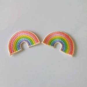 以下が含まれることがあります： 虹色のアーチ型の刺繍パッチが2つ。パッチは白い背景の上にあります。