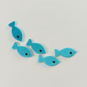 May include: Five turquoise blue felt fish with black eyes, arranged in a row, on a white background.