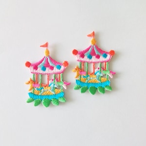 May include: A pair of colourful embroidered carousel horse earrings. The earrings are pink, blue, green, yellow, and orange. The horses are on a carousel with a pink and blue roof.