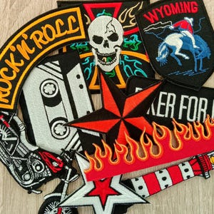 May include: A collection of embroidered patches featuring a black and white cassette tape, a skull with colorful patterns, a Wyoming bucking horse, a red and black star, a motorcycle, a lighthouse, and a curved patch with the text ROCK'N'ROLL.