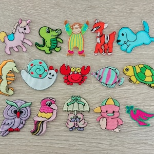 May include: A collection of fourteen embroidered fabric patches featuring various colorful designs including a pink pony, green crocodile, monkey, red fox, blue dog, seahorse, snail, red crab, striped fish, turtle, purple owl, parrot, ducks, and a bird.