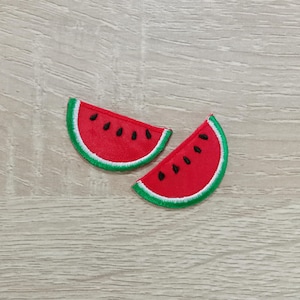 May include: Two watermelon slice patches. Each patch features a red interior with black seeds, a white border, and a green rind. These patches are perfect for adding a touch of summer to clothing or accessories.