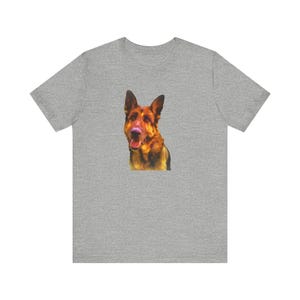 May include: A heather gray t-shirt featuring a close-up of a German Shepherd dog's face. The dog has brown and black fur with a pink nose and open mouth. The t-shirt is made of a soft material.