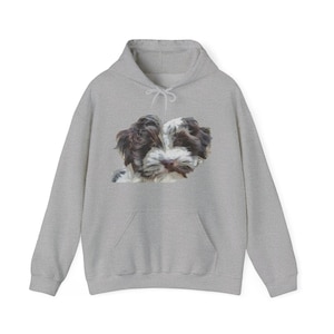 May include: A light gray hoodie featuring a detailed image of a small dog's face. The dog has brown and white fur, with a fluffy appearance. The hoodie has a kangaroo pocket and a drawstring hood.