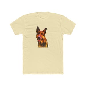 May include: A light yellow t-shirt featuring a detailed illustration of a German Shepherd dog's head. The dog has brown and black fur with its tongue slightly visible. The shirt is made of a soft material.