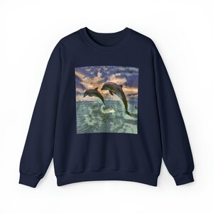 Könnte beinhalten: Ein marineblaues Sweatshirt mit einem grafischen Druck von zwei Delfinen, die aus dem Wasser springen. Die Delfine sind vor einem blauen Himmel mit Wolken silhouettiert. Das Wasser ist hellblau und grün.