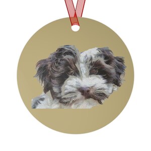 May include: A round gold ornament with a white and brown puppy dog with black eyes looking at the camera.