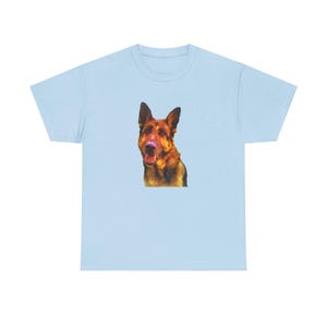 May include: Light blue t-shirt featuring a graphic of a German Shepherd dog. The dog has brown and black fur with its tongue slightly out. The t-shirt is a classic crew neck style.
