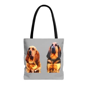 Puede incluir: Un bolso tote gris con dos retratos de perros Bloodhound estilo acuarela. Los perros están representados en tonos marrones, negros y beige. El bolso tiene asas negras y un fondo gris claro.