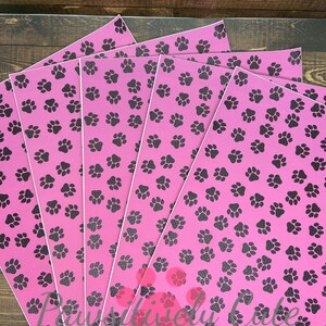 May include: Five sheets of pink vinyl with a black paw print pattern. The sheets are stacked on top of each other.