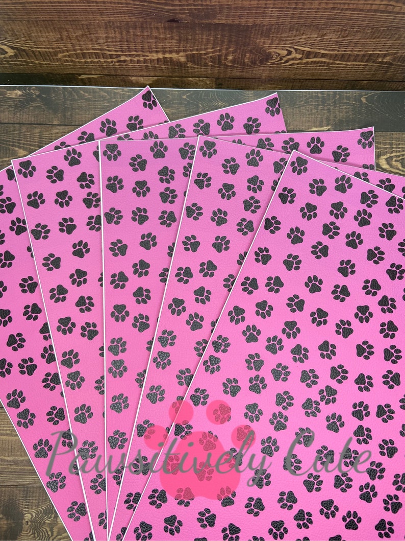 May include: Five sheets of pink vinyl with a black paw print pattern. The sheets are stacked on top of each other.