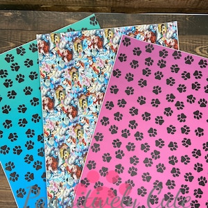 May include: Three sheets of patterned fabric. One sheet is teal with black paw prints, one sheet is pink with black paw prints, and one sheet is blue with a multi-coloured pattern of dogs and other animals.