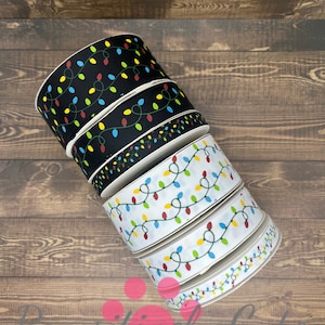 May include: A stack of five rolls of black and white ribbon with a Christmas lights pattern. The lights are red, yellow, green, and blue.