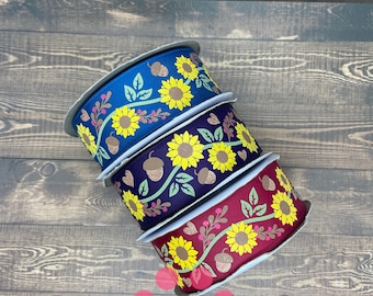 May include: Three rolls of ribbon with a sunflower and acorn design. The ribbon is in shades of blue, purple, and red.