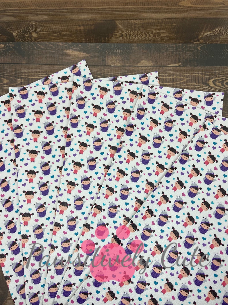 May include: A stack of white fabric sheets with a repeating pattern of a cartoon girl wearing a purple costume and a crown. The girl is surrounded by small purple, pink, and blue hearts.