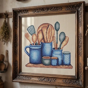 Peut inclure: Broderie au point de croix encadrée dans un cadre en bois. L'image représente des ustensiles de cuisine et un pain dans des récipients en céramique bleus. Cuillères en bois, spatules et rouleau à pâtisserie sont visibles. L'œuvre est sur fond neutre.