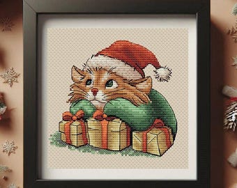 May include: Cross-stitch art of a ginger cat wearing a Santa hat and green sweater, resting on three wrapped gifts with red bows. The artwork is framed in a black square frame, perfect for Christmas decor.
