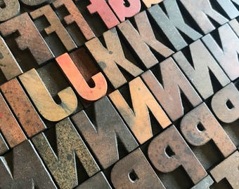 May include: A close-up of a collection of wooden letterpress blocks, arranged in a staggered pattern. The blocks are painted in various shades of brown, with some blocks painted in red. The letters "J", "L", "G", and "F" are visible.