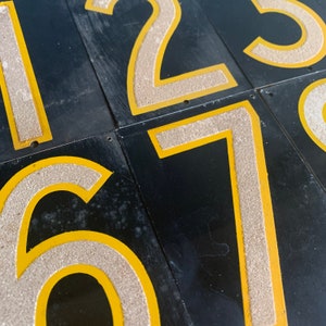 May include: Close-up of black rectangular tiles featuring the numbers 1, 2, 3, 6, and 7. The numbers are light beige with a textured finish, outlined in yellow. The tiles are arranged in a grid.