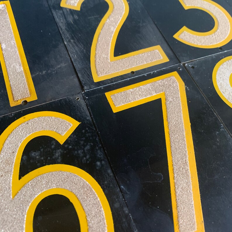 May include: Close-up of black rectangular tiles featuring the numbers 1, 2, 3, 6, and 7. The numbers are light beige with a textured finish, outlined in yellow. The tiles are arranged in a grid.