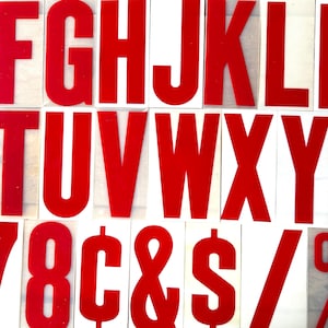 May include: Red plastic letters and symbols, including the alphabet, numbers, dollar sign, ampersand, and a forward slash. The letters and symbols are arranged in rows on a white background.