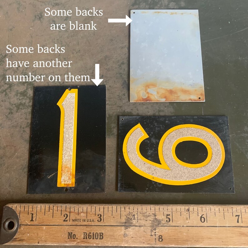May include: Vintage metal number signs with black backgrounds and yellow trim. The numbers "1" and "9" are visible, with a blank metal sign and a ruler in the image. The text "Some backs are blank" and "Some backs have another number on them" is also visible.