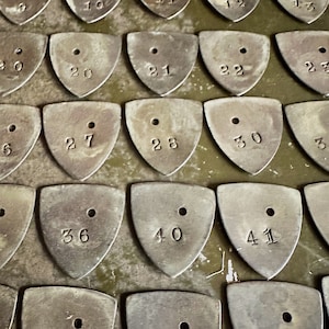 May include: A close-up of a collection of metal tags with numbers ranging from 6 to 41. The tags are triangular in shape and have a small hole in the center. The tags are arranged in rows on a green surface.