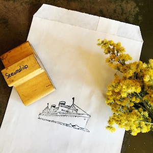 May include: A white paper bag with a wooden stamp that says "Steamship" and a black and white illustration of a steamship. A bouquet of yellow flowers is in the upper right corner of the image.