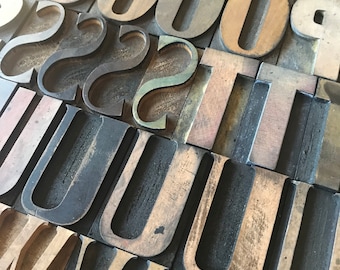 May include: Close-up of a collection of vintage wooden letterpress printing blocks. The blocks are arranged in a random pattern and feature the letters O, S, U, and T. The blocks are made of dark wood and have a worn, aged appearance.