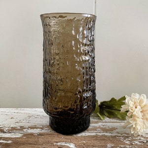 May include: A brown glass vase with a textured surface. The vase is sitting on a wooden surface.