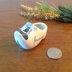 May include: A small white ceramic Dutch shoe with blue and black painted details of a windmill and the word "Holland".