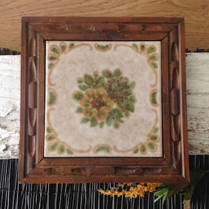 May include: A wooden framed tile trivet with a floral design in shades of green, brown, and orange. The tile is white with a decorative border.