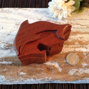 May include: A wooden dolphin shaped puzzle box with a dark brown finish. The box is open and the inside is visible. A US penny is placed next to the box for scale.