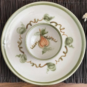 May include: A white ceramic serving platter and bowl set with a green rim and painted pear and leaf design. The pear is orange and brown, with green leaves and brown vines. The set is perfect for serving appetizers.