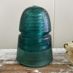 May include: A teal blue glass insulator with a rounded top and a textured surface. The insulator is made of glass and has a vintage look.