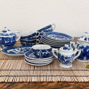 May include: A miniature tea set featuring a blue and white willow pattern. The set includes a teapot, two lidded sugar bowls, several teacups with matching saucers, and small plates. Each piece is decorated with detailed landscape illustrations.